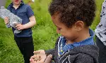 Two young children outdoors, one holding a stuffed animal and one gently holding a live frog